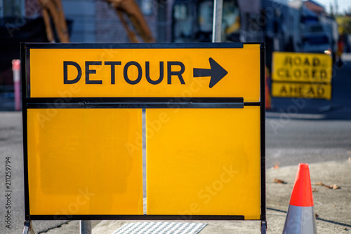 A yellow road sign with the word DETOUR and a arrow pointing to the right.