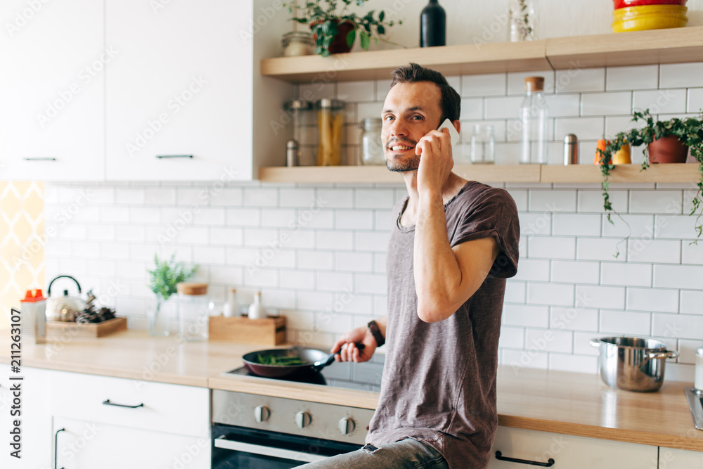 Portrait of brunet man with frying pan in his hands talking on phone in kitchen Portrait of brunet man with frying pan in his hands talking on phone in kitchen