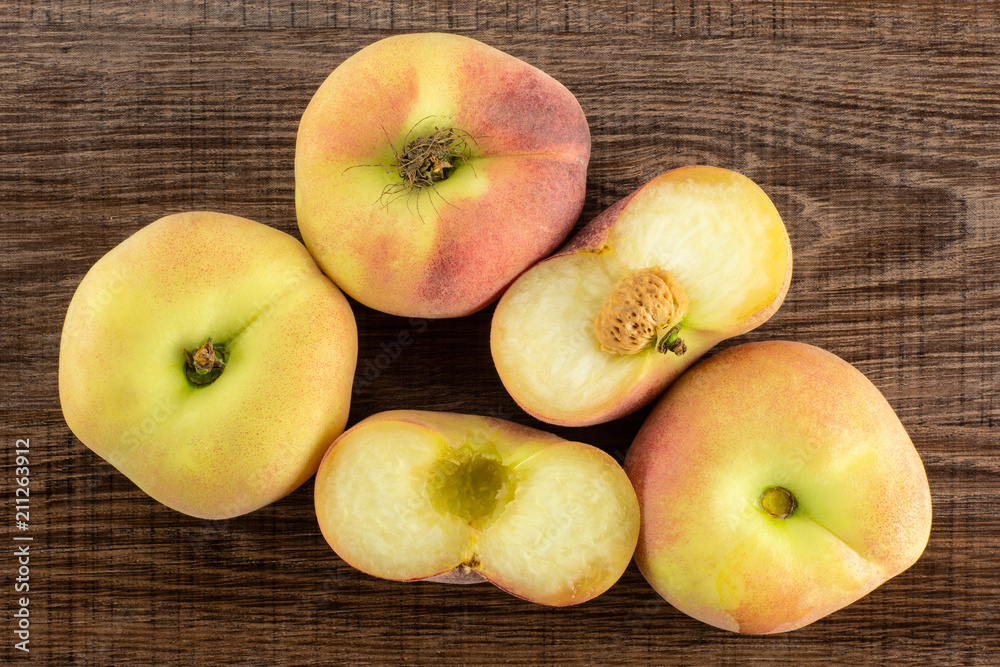 Three fresh ripe Saturn peaches and one cut in two halves top view on brown wood background. Three fresh ripe Saturn peaches and one cut in two halves top view on brown wood background.