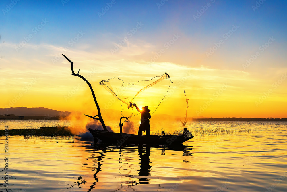 Silhouette of asian fisherman on wooden boat ,fisherman in action throwing a net for catching freshwater fish in nature river