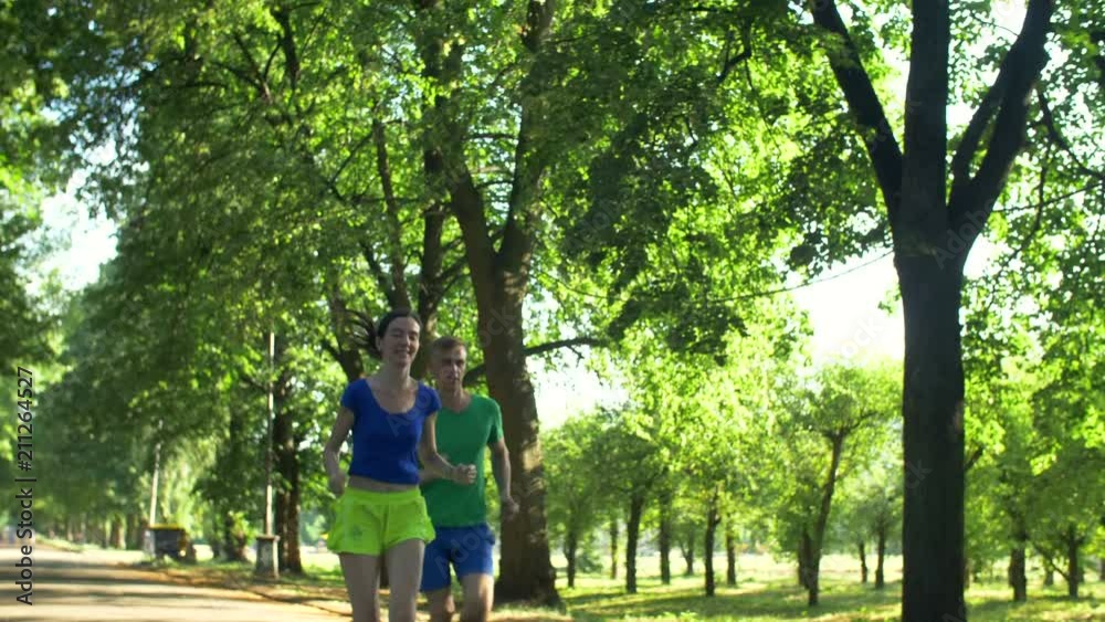 Positive athletic sporty male jogger outrunning charming female runner on park trail during jogging. Cheerful healthy man overtaking beautiful female jogger during running in summer park. Positive athletic sporty male jogger outrunning charming female runner on park trail during jogging. Cheerful healthy man overtaking beautiful female jogger during running in summer park.
