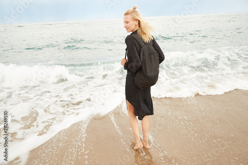 A blonde girl is stepping inside the Mediterranean sea enjoying the water, waves and drops in Barcelona