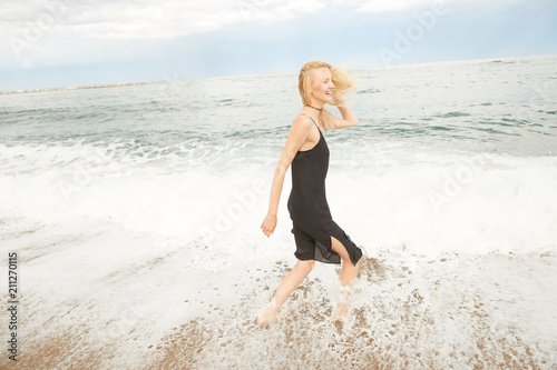 A blonde girl is stepping inside the Mediterranean sea enjoying the water, waves and drops in Barcelona