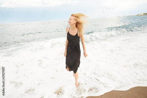 A blonde girl is stepping inside the Mediterranean sea enjoying the water, waves and drops in Barcelona