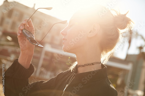 Beautiful blonde model girl putting off her sunglasses on the street in sunset