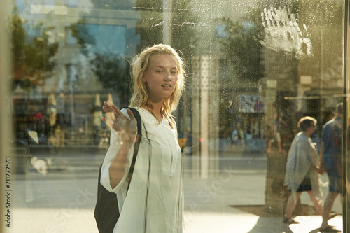 Ablonde model girl passing bus stop on the street, view through glass