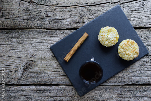 Two muffins covered with shtryzelem and cheesecream on a black board, next to a cup of coffee and a cinnamon stick on a wooden background photo