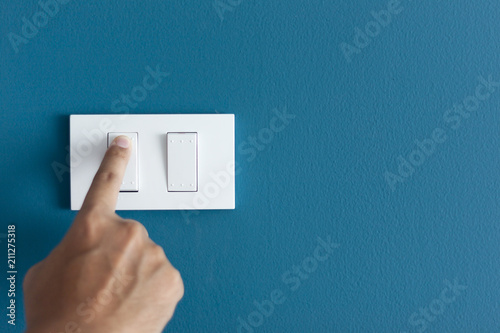 A finger turning on lighting switch on rough on blue dark wall. photo