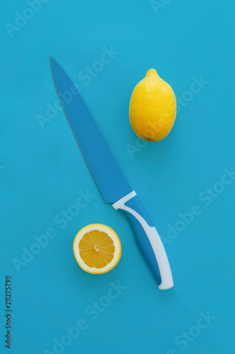 yellow lemon, slice of lemon and knife on bright blue paper, trendy flat lay. fruits modern image, top view. juicy summer vitamin eat and diet concept. pop art style. creative minimalism photo