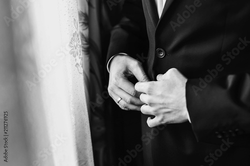 groom putting on stylish black suit , white shirt and bow tie. man hands. morning preparations before wedding day. groom outfit. getting ready. black and white