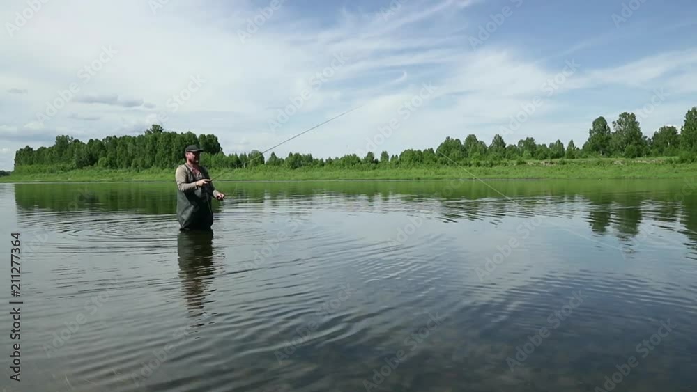 Joyful fisherman is fishing in calm river water near the shore Joyful fisherman is fishing in calm river water near the shore