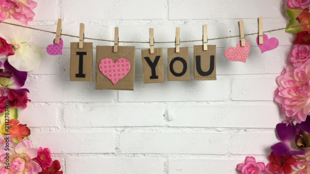 Frase “I love you” colgando de una cuerda con pinzas, rodeado de flores.