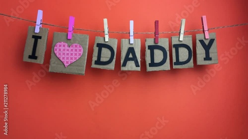 Frase “I love daddy” colgando de una cuerda con pinzas sobre fondo naranja. photo