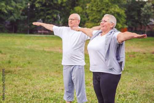 senior couple are outdoors in a park exercise with dumbbells and having fun together.