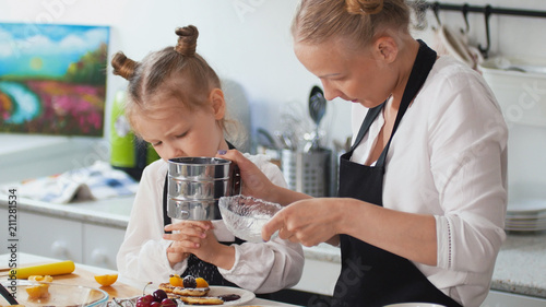 Woman with her child puts sugar in the pancakes