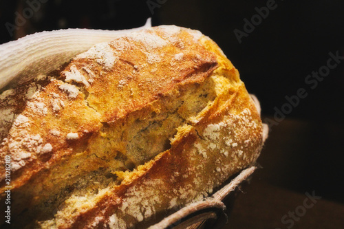 Freshly baked rustic white wheat flour bread loaf roll in a basket against a black background