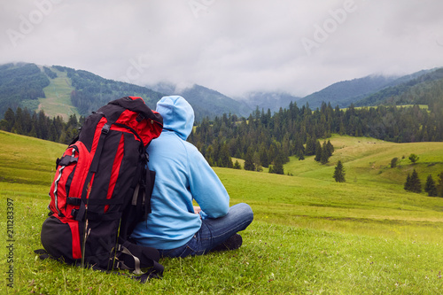 Hill walker is sitting in the middle of mountain wilderness. Traveler man in the field. Man with backpack hiking in mountains Travel Lifestyle success concept adventure active vacations outdoor 