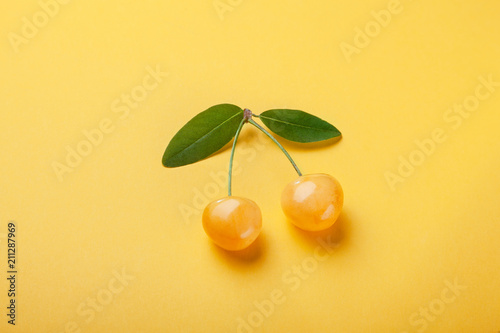Two yellow cherries with green leaf on  yellow background, good postcard.