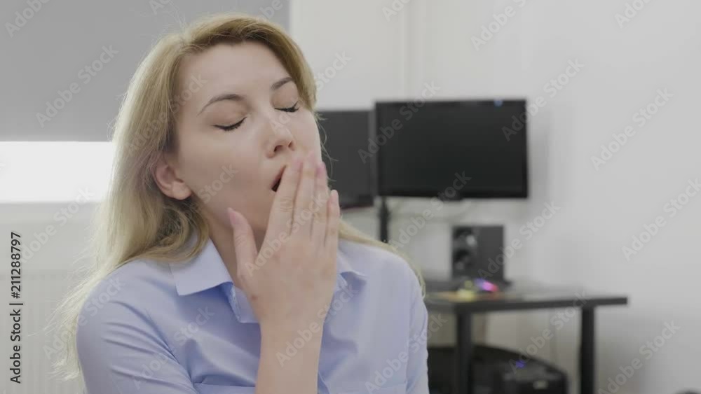 Blonde young sleepy employee at office desk yawning looking bored and tired Blonde young sleepy employee at office desk yawning looking bored and tired