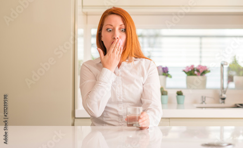 Thirsty redhead woman and glass of water cover mouth with hand shocked with shame for mistake  expression of fear  scared in silence  secret concept