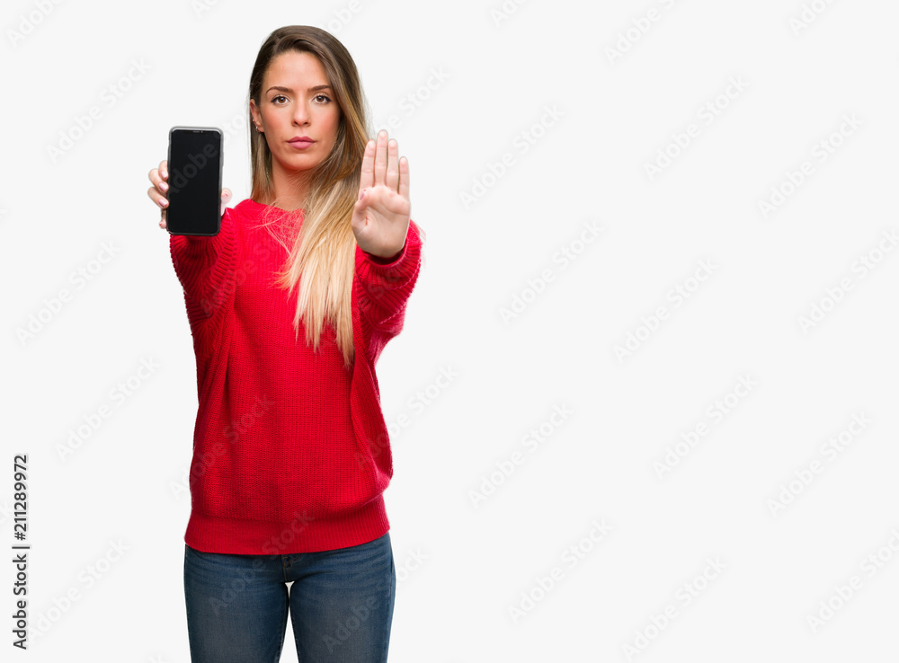 Beautiful young woman using smartphone with open hand doing stop sign with serious and confident expression, defense gesture Beautiful young woman using smartphone with open hand doing stop sign with serious and confident expression, defense gesture