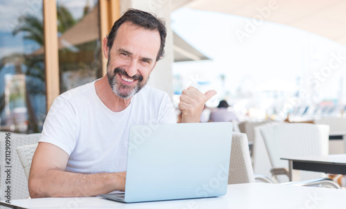 Handsome senior man using laptop at restaurant pointing with hand and finger up with happy face smiling