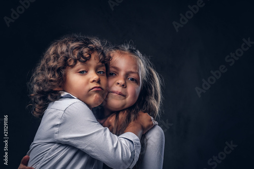 Cute couple of a little boy with curly hair and beautiful girl have fun at a studio. Isolated on a dark textured background.