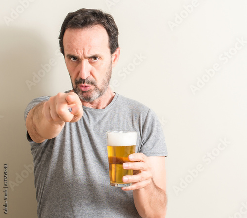 Senior man drinking beer pointing with finger to the camera and to you, hand sign, positive and confident gesture from the front