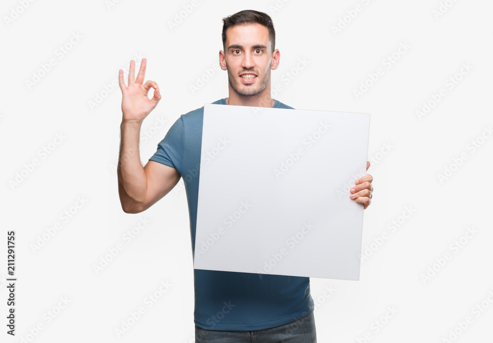 Handsome young man holding advertising banner doing ok sign with fingers, excellent symbol