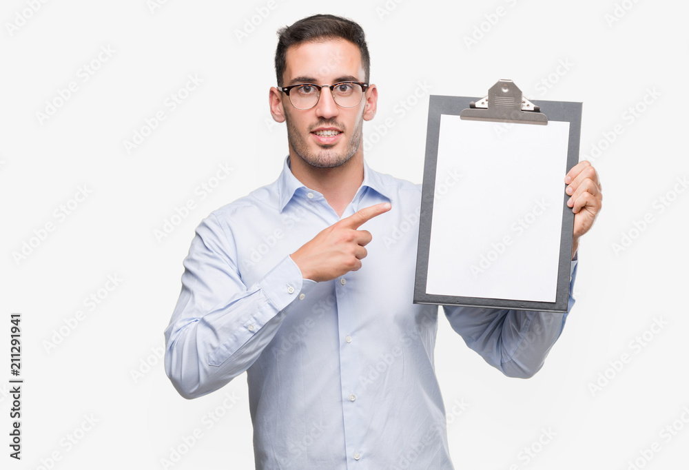 Handsome young business man showing a clipboard very happy pointing with hand and finger