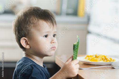 the child in the kitchen eating fresh cucumber and omelet