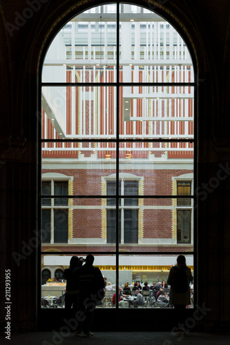 Amsterdam, Netherlands - May 2018: People looking trought a big window to the visitors in modern main hall in the new atrium of the Rijksmuseum. Entrance to museum, massive ceiling decorations and