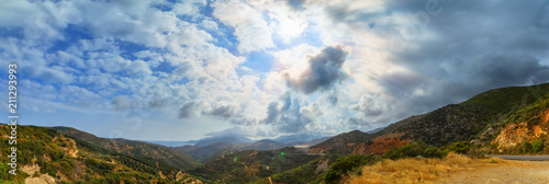 panorama view of the mountains, storm clouds and sun with rays on beach, Crete Greece