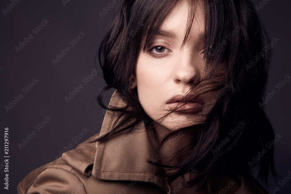 Dark close up portrait of beautiful sensual and hot woman with nude makeup, dark hair, wearing beige trench coat. Studio shot Dark close up portrait of beautiful sensual and hot woman with nude makeup, dark hair, wearing beige trench coat. Studio shot