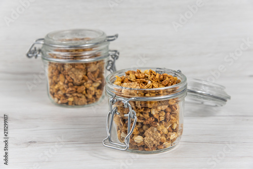 Two jars full of granola  on the white wood table