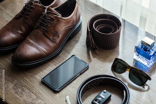 Different men's accessories such as: shoes, belt, tie, glasses, car keys and telephone - are on the table