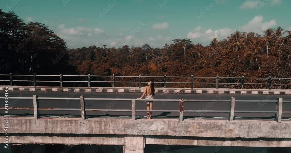 Aerial drone view of the girl standing on the bridge. View of rainforest canyon and bridge in Bali, Indonesia - colored viideo