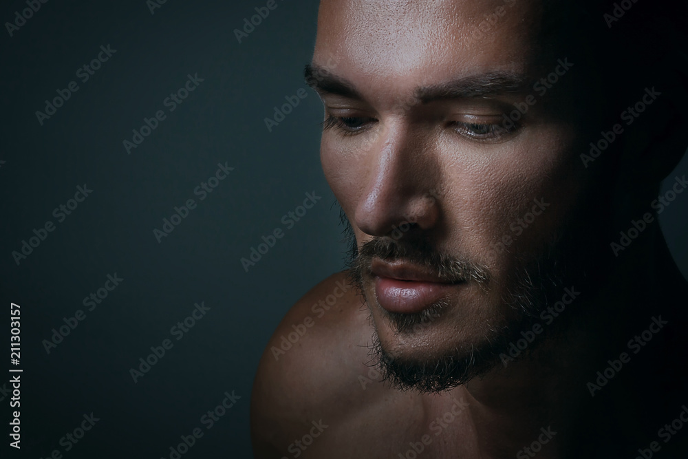 Close up portrait of a handsome young man with brave manly face on dark background. Caucasian man staring serious, male beauty, cosmetics.