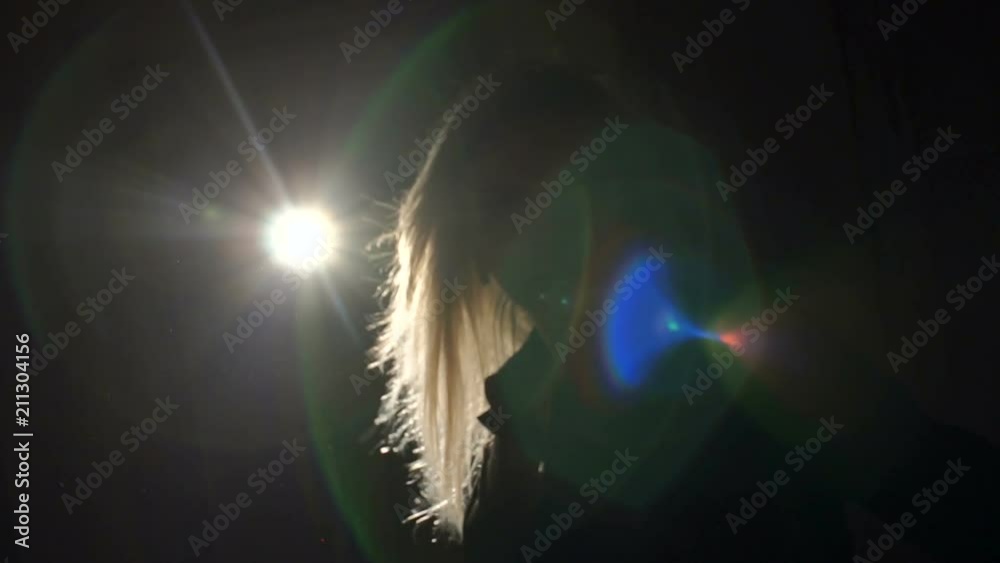 Portrait of a young blonde woman in the light of a bright spotlight in the dark. Slow motion. Silhouette. Portrait of a young blonde woman in the light of a bright spotlight in the dark. Slow motion. Silhouette.