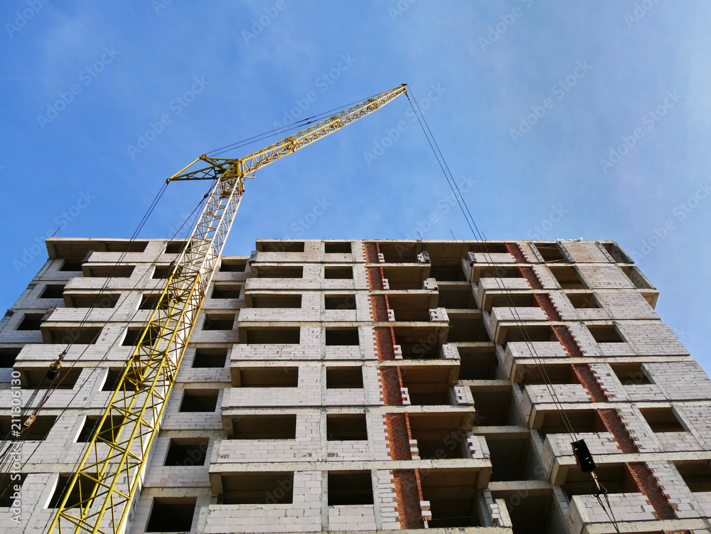 Naklejka premium Concrete building under construction. Industrial crane near building. Construction site.