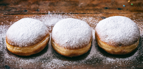  Krapfen with powder sugar, three and isolated on wooden background.