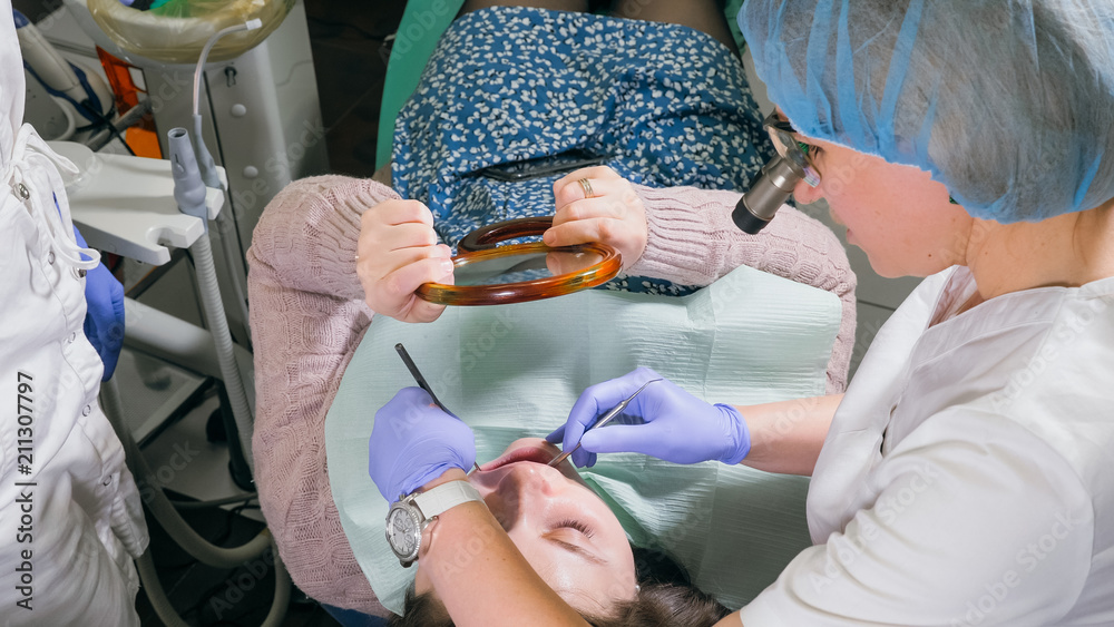 Woman at dentist clinic gets dental treatment to fill a cavity in a tooth. Dental restoration and composite material polymerization with UV light and laser. The patient looks in the mirror.