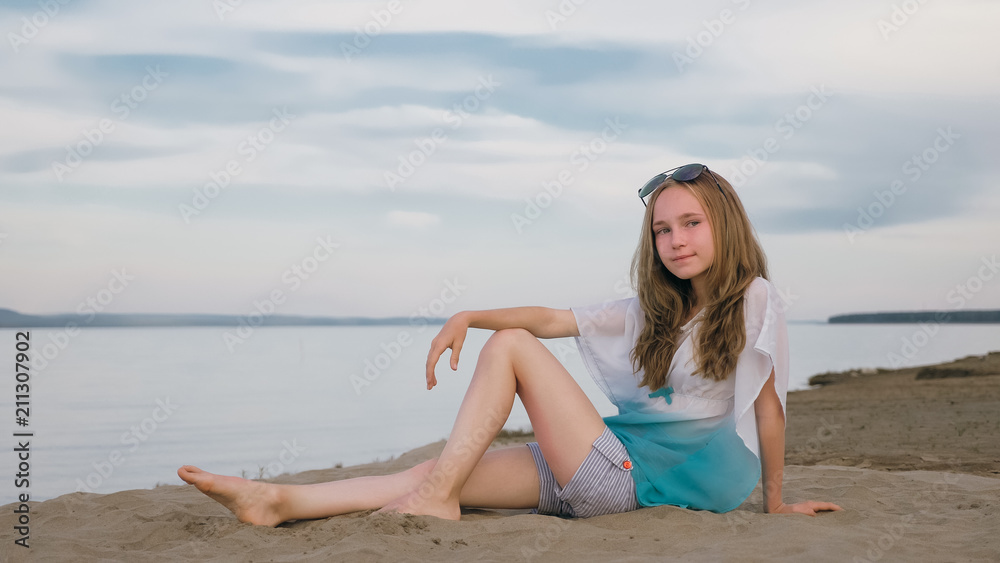 One beautiful teenage girl with brown hair outside on a beautiful summer day. The woman is sitting on the beach. The sun was gone in the sunset. One beautiful teenage girl with brown hair outside on a beautiful summer day. The woman is sitting on the beach. The sun was gone in the sunset.