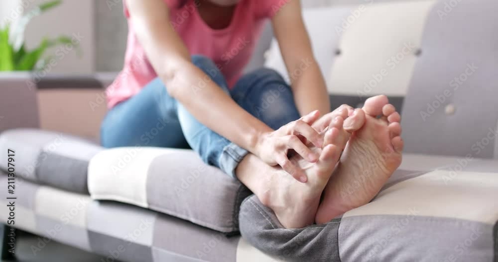 Woman feeling itchy on feet and sitting on sofa