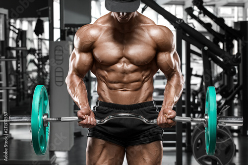 Muscular man working out in gym doing exercises with barbell for biceps, strong male naked torso abs