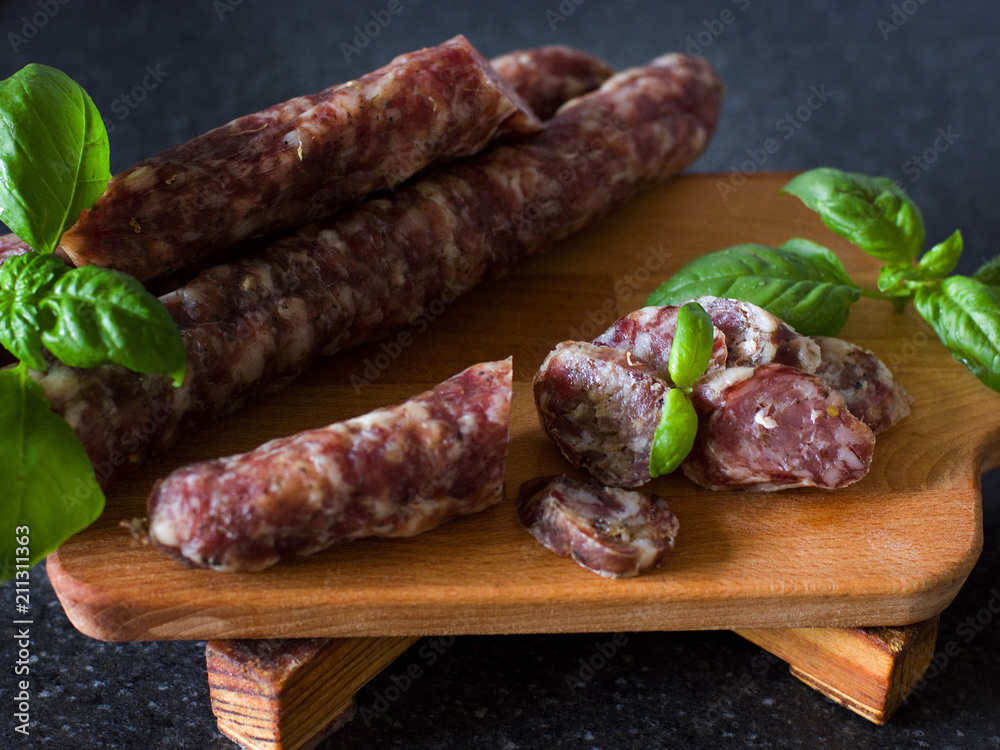Dry homemade sausage on a wooden background decorated with a green basil on a gray background. Soft focus.