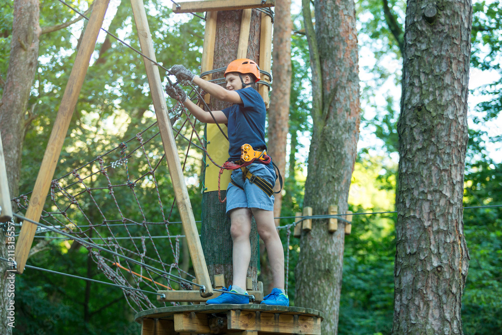 cute sporty 10 year boy is doing activity in adventure rope park with all climbing equipment like helmet, rope and carabiner. summer camp, active lifestyle concept cute sporty 10 year boy is doing activity in adventure rope park with all climbing equipment like helmet, rope and carabiner. summer camp, active lifestyle concept