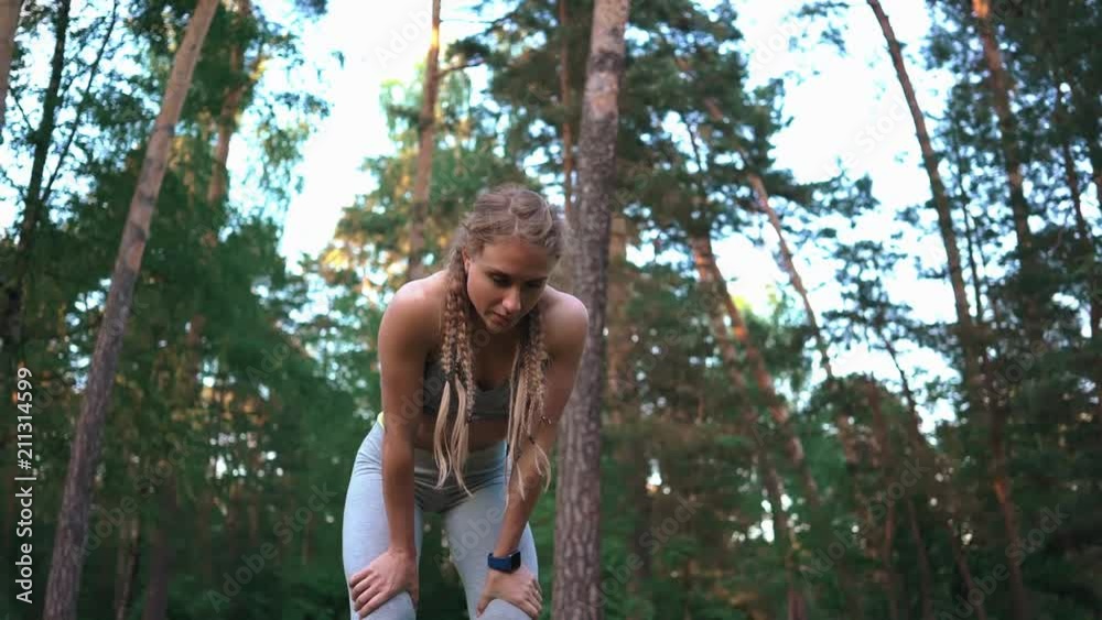 Gorgeous fit young woman with long braided hair resting and breathing heavily after her cardio workout in the woods in summer. Left to right pan slow motion medium shot Gorgeous fit young woman with long braided hair resting and breathing heavily after her cardio workout in the woods in summer. Left to right pan slow motion medium shot