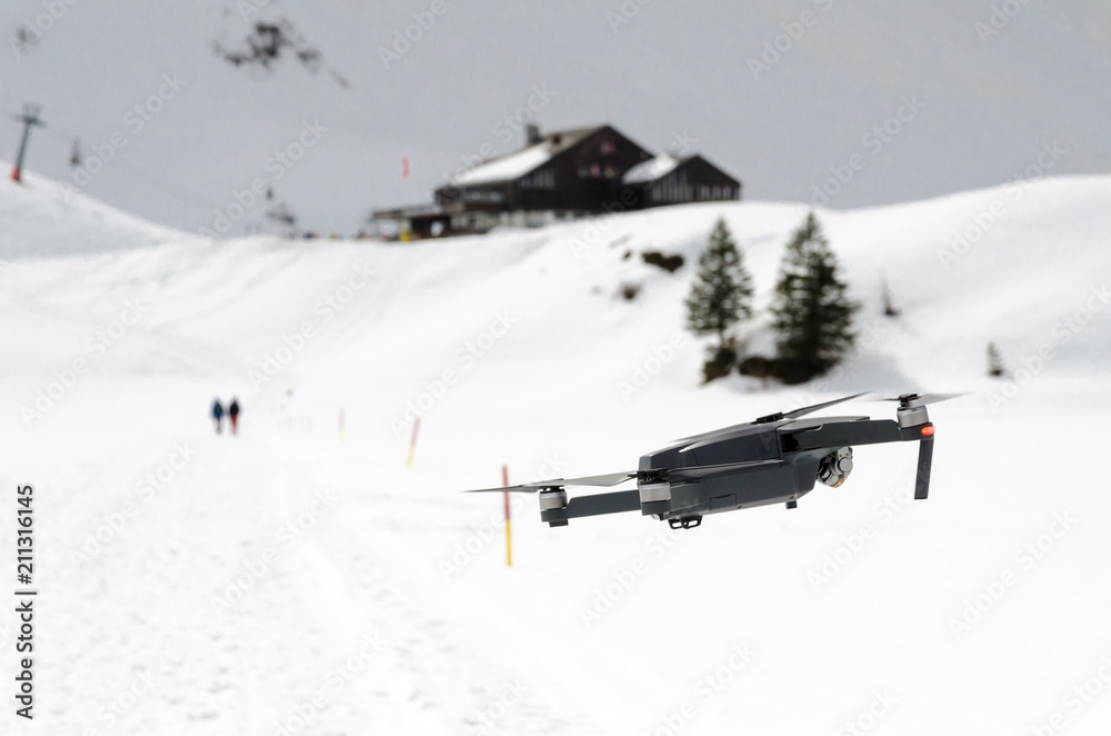 A camera drone hovering and flying over snowy skiing hills in alps