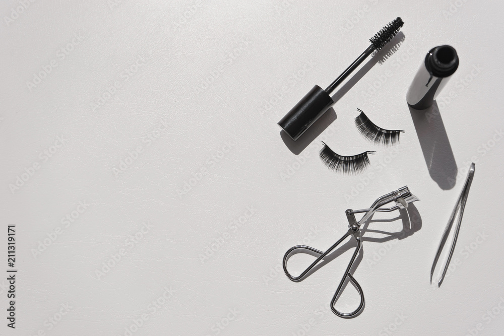 Black false lashes strips, mascara, tweezers, curler on white background Black false lashes strips, mascara, tweezers, curler on white background